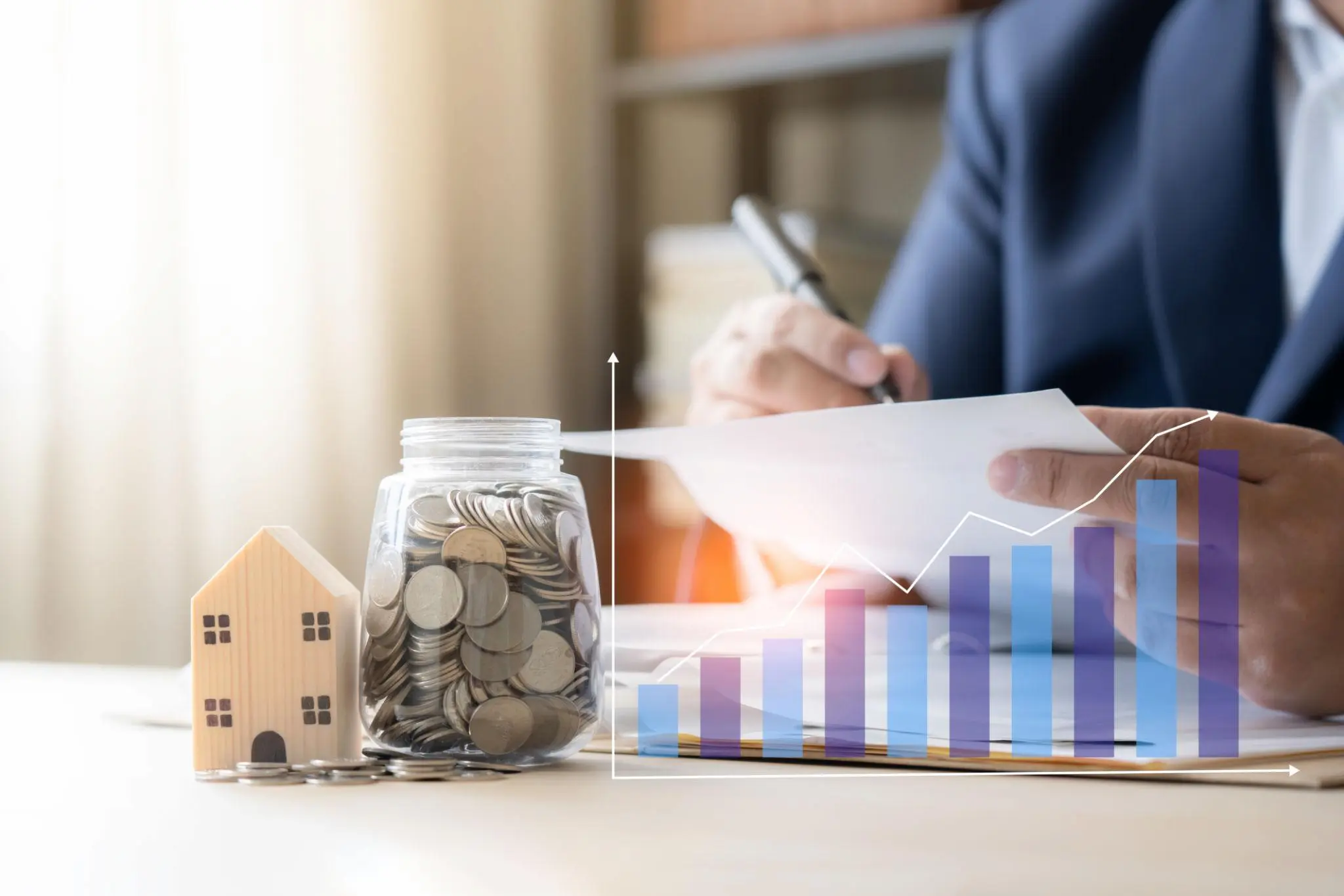 Real estate professional reviewing financial growth charts beside a model house and a jar of coins.